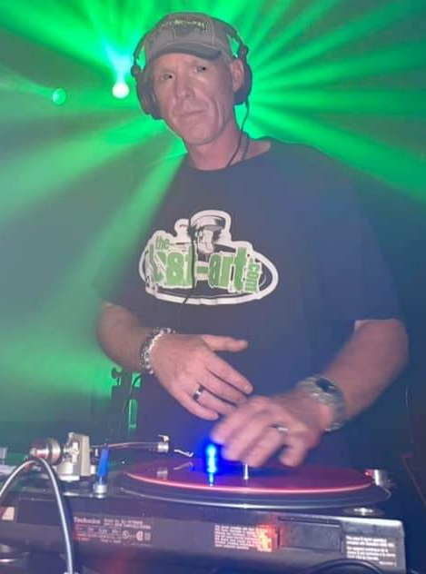 DJ Natural Nate® in DC hat and BYBB white tee, deep bend scratch action on Technics turntable